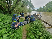 Einsatzkräfte des Technischen Hilfswerks befinden sich an einem Fluss. Zwischen sich liegt eine Krankentrage.